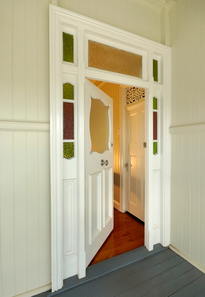 An image of a front door with stained glass above the door and colonial-style casing. 