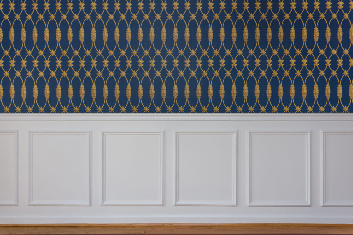 White chair rail complements the ornate dark blue and gold wallpaper above it and the hardwood floors below it.