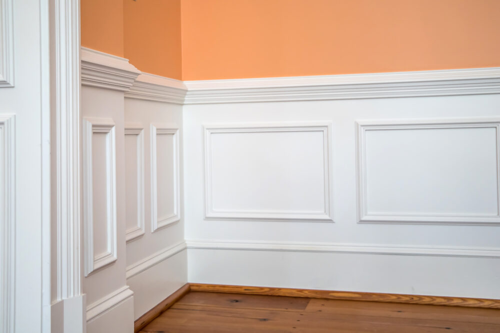 An orange wall with a white chair rail to separate it from the hardwood floors.