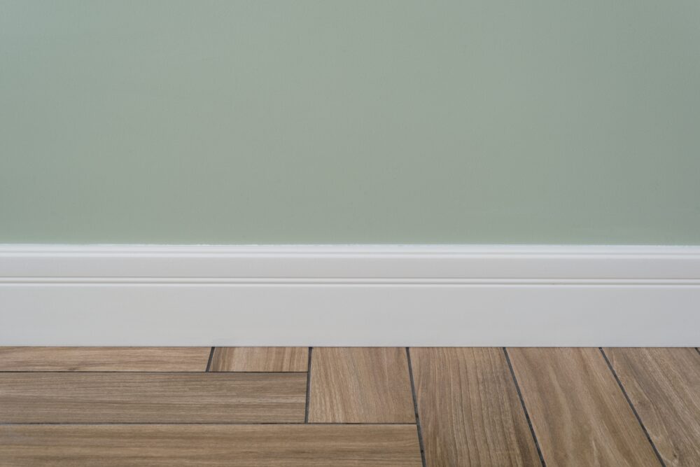 An image of a light green wall transitioning to the wooden floor with a white baseboard trim.