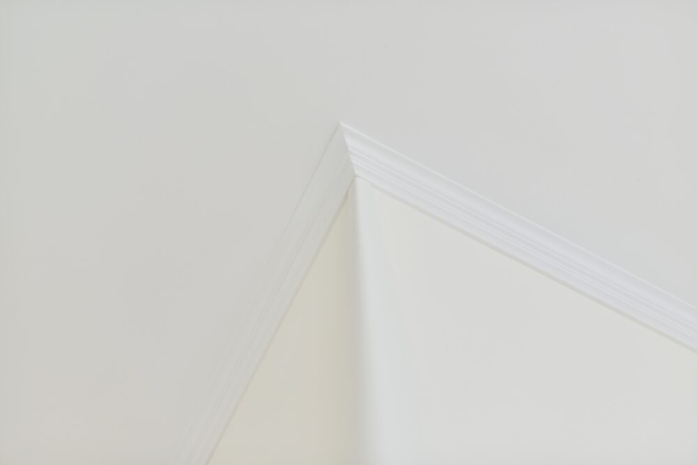 An image of white crown moulding that seamlessly blends where the white ceiling and the off-white walls meet. 