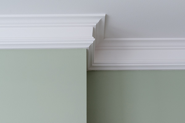 A image of crown moulding connecting a green wall and a gray ceiling
