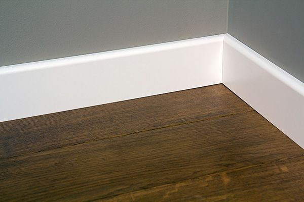 An image of a baseboard connecting a hardwood floor and a gray wall