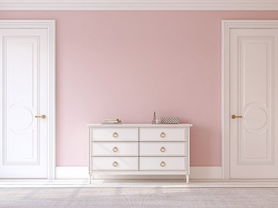 Two white doors with white door casings in a pink hallway, separated by a dresser.
