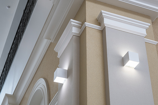 An image of white moulding on tan walls and small, square lights just under the moulding.
