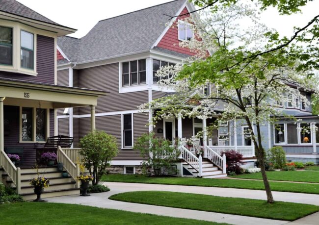 Row of painted wood homes with white window casing, porch columns and trimmed gables